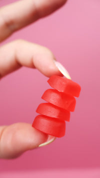 Gummies rouges en forme de pastilles empilées, tenues par deux doigts.
