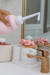 Douchette nomade intime rose, eau qui s’écoule depuis l’embout blanc