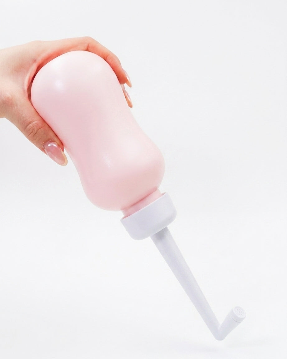 Douchette nomade intime rose, tenue en main, embout blanc et flexible court